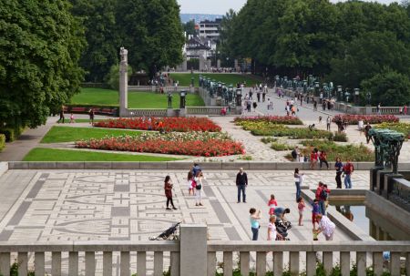 Hovedinngangen til Frognerparken i bakgrunnen. Foran er mange mennesker, blomsterbed og skulpturer
