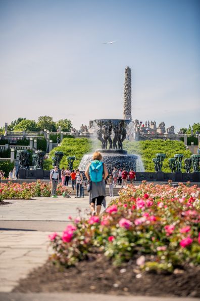 Monolitten med flere skulpturer foran. Blomsterbed og mennesker