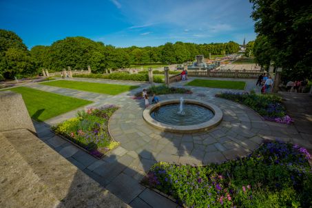 Utsikt over Frognerparken på sommerstid. Grønt gress, blomster, mange mennesker.
